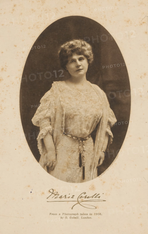 Portrait of Marie Corelli, photomechanical print, name: 'Marie Corelli', copyright notice: 'G. GABELL. COPYRIGHT.', inscription: 'From a Photograph taken in 1906, . by G. Gabell, London.', photographer: G. Gabell, London, clichémaker: anonymous, in or after 1906, paper, rotogravure, height 124 mm x width 82 mm, Person, Marie Corelli, portrait of a writer, An oval sepia photograph shows a woman standing and facing slightly toward the camera, wearing a light-colored dress with lace and embroidered details and loose flowing sleeves, a tasseled belt around her waist, short curly hair, a neutral facial expression, and her hands resting by her sides against a dark background framed by a lighter mottled border.