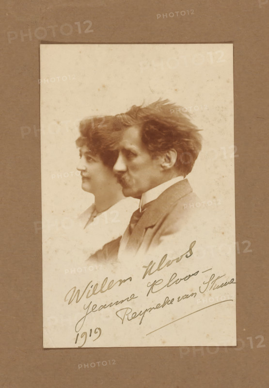 Portrait of Jeanne Henriette Reine Reyneke van Stuwe and Willem Kloos, photograph, name: 'Willem Kloos, Jeanne Kloos-, Reyneke van Stuwe, 1919', inscription: 'HC DEN DRYVER.', photographer: Hendrik Cornelis den Drijver (signed by artist), The Hague, 1919, paper, pasteboard, matte daylight collodion silver print, height 140 mm x width 89 mm, Person, Jeanne Henriette Reine Reyneke van Stuwe, Willem Kloos, writer, poet, author, A sepia-toned photograph mounted on a darker mat shows two portrait profiles overlapping, a woman positioned slightly behind a man; the woman has short wavy hair and a soft expression, wearing a light-colored garment with a visible collar, while the man in front has tousled hair, a mustache, and is dressed in a suit jacket with a shirt and tie. The photographic paper displays age spots and slight discoloration. The darker mat frames the lighter photograph with a narrow border visible around its edges.