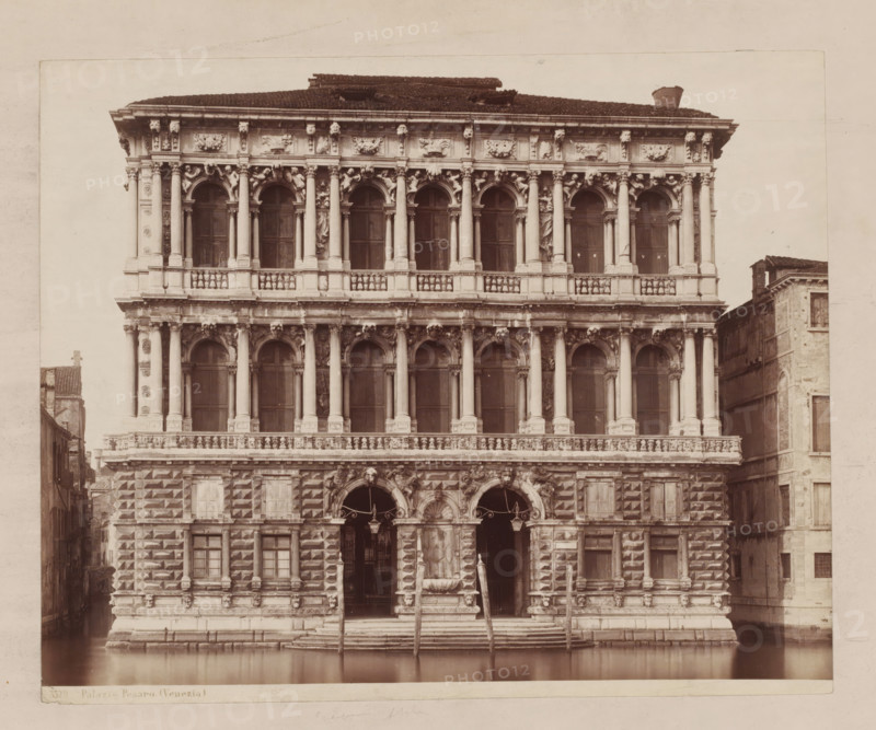 Palazzo Pesaro (Venezia), View of the Palazzo Pesaro in Venice, Italy, photograph, inscription: 'Pl. 9 style h', number: '32', inscription: 'II', inscription: 'pal Pesaro in Venice, ...', number: 'No. 3529.', collector's mark: 'RIJKS SCHOOL FOR ART NIJVERINGEN, GROEP', photographer: attributed to Giorgio Sommer, Venice, 1857 - 1914, Giorgio Sommer, photographer, Attributed to, pasteboard, paper, albumen print, albumendruk, height 321 mm x width 479 mm, hôtel, ie small palace in city, Ca' Pesaro, A large ornate stone façade with multiple levels of arched windows and columns faces a calm canal, showing decorative sculptures and reliefs between the columns and above the arches; the lower section features rusticated masonry with square protruding blocks, two tall arched doorways with decorative surrounds and a central fountain basin flanked by stone steps leading down to the water, where wooden mooring poles rise from the canal; the upper stories display paired columns, balustrades, and sc...