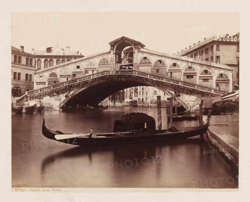Venezia. Ponte Rialto, View of the Ponte Rialto in Venice, Italy, photograph, collector's mark: 'RICH SCHOOL FOR ARTISTS, GROUP', number: 'No. 3522.', number: '37', photographer: attributed to Giorgio Sommer, Venice, 1857 - 1914, Giorgio Sommer, photographer, Attributed to, pasteboard, paper, albumen print, albumendruk, height 319 mm x width 479 mm, landscape with bridge, viaduct or aqueduct, canals, waters (in city), gondola, Canal Grande, Ponte Rialto, A stone arch bridge with decorative balustrades spans a canal, flanked by buildings with arched windows and shutters; gondolas float in the water beneath and in the foreground, one with a covered cabin and carved prow is moored near a stone quay with wooden posts and canopied stalls visible along the right bank.