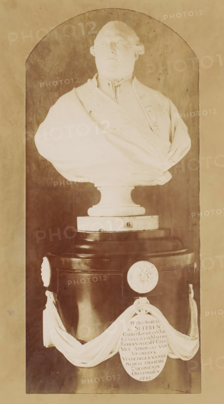 Bust of Pierre André de Suffren de Saint-Tropez, photograph, after sculpture by Jean Antoine Houdon, 1890 - 1920, Jean Antoine Houdon, photographer, after sculpture by, paper, pasteboard, baryta paper, gelatin silver print, developing gelatin silver print, height 283 mm x width 158 mm, Person, Pierre André de Suffren de Saint-Tropez, piece of sculpture, reproduction of a piece of sculpture, historical persons, A marble bust of a man with a high collar and draped garment sits on a rounded pedestal within an arched niche, the bust showing facial features, hair styled back, and a sash across the chest; the pedestal has a dark cylindrical base with decorative round medallions and a draped cloth element hanging in front, and the overall scene is in warm sepia tones with visible surface texture on the niche walls.