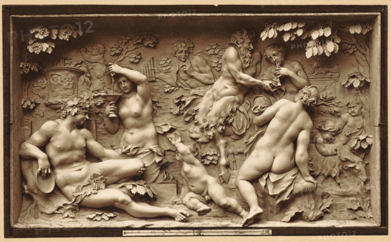 Hautrelief in Elfenbein von J. Elhafen. 1710. Bacchanale, Ivory relief depicting a bacchanal, by Ignaz Elfhafen, photomechanical print, number: 'Blatt 180.', Germany, cliché maker: anonymous, after sculpture by Ignaz Elhafen, printer (person): attributed to Johann Baptist Obernetter, Munich, 1869 - 1887, Ignaz Elhafen, photographer, clichémaker, after sculpture by, printer (person), Bavaria, Attributed to, pasteboard, paper, collotype, photoprint, height 130 mm x width 214 mm, height 418 mm x width 538 mm, piece of sculpture, reproduction of a piece of sculpture, bacchanal: Bacchus with his wine-flushed train (thiasos), A rectangular relief framed by a border shows a group of sculpted figures in a natural setting with leaves and grapes along the top corners. On the left a reclining male figure wearing a wreath and holding a circular dish rests against a carved seat, next to a standing female figure who holds a shallow cup and raises one hand to her head. In the center a small child rea...