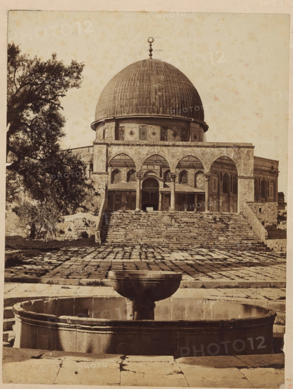 Mosque of Omar., View of the Dome of the Rock Mosque in Jerusalem, photograph, inscription: 'Omar Mosque Jerusalem', Jerusalem, c. 1875 - c. 1900, photographer, paper, pasteboard, albumen print, albumendruk, height 250 mm x width 188 mm, utilitarian, public pump or water fountain, dome, architecture, temple, shrine, non-Christian religions, Dome of the Rock, A sepia-toned photograph showing a large domed building with a rounded roof topped by a decorative finial, a colonnaded façade with arches, and a broad flight of worn stone steps leading up to the entrance; in front of the steps a paved courtyard with irregular stone slabs is visible, and a circular stone fountain basin with a raised central bowl sits in the foreground; a large tree with dense foliage occupies the left side of the image, and the building’s exterior shows patterned panels and window openings beneath the dome.