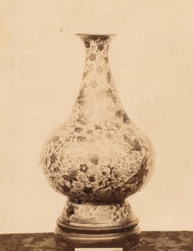 Vase decorated with floral motif and butterflies, photograph, number: '4.', c. 1875 - c. 1900, photographer, paper, pasteboard, albumen print, albumendruk, height 257 mm x width 199 mm, flowers, ornament, insects: butterfly, container of ceramics: jar, jug, pot, vase, ornamenting, decorating, applied arts, A tall, rounded vase with a narrow neck and flared rim sits on a short pedestal base, both covered in a dense floral pattern of small blossoms and curling vine motifs; the surface shows areas of darker staining and wear, and the image has a warm, sepia tone with a plain, lightly mottled background.