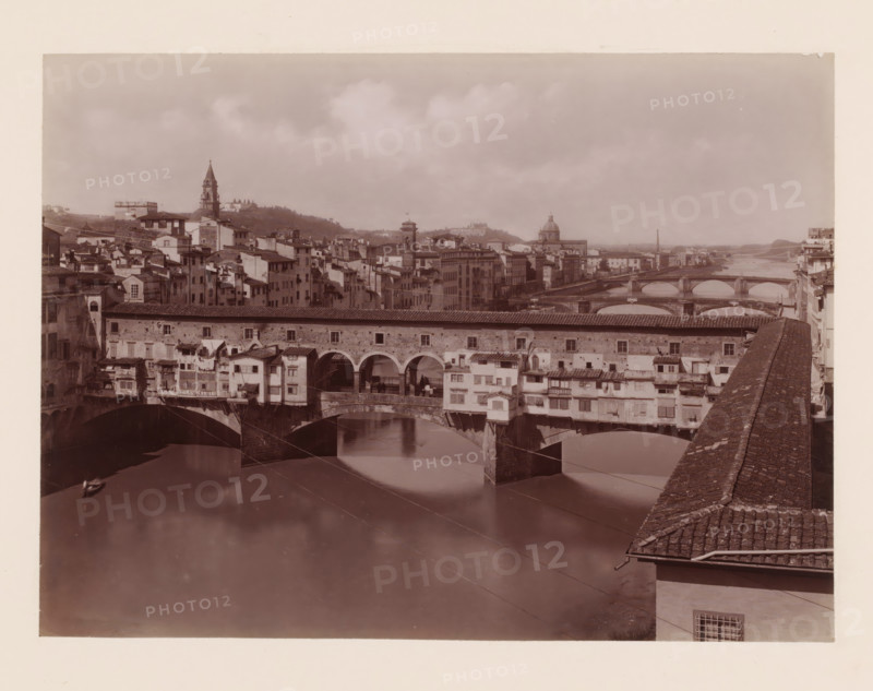 Ponte Vecchio, rifondato nel 1355 coll'opera di Taddeo Gaddi, Ponte Vecchio over the Arno in Florence, Italy, Firenze, photograph, number: '10.', number: '3066.', photographer: Giacomo Brogi (possibly), Florence, publisher: attributed to Edizioni Brogi, 1864 - 1881, Giacomo Brogi, Edizioni Brogi, photographer, publisher, Tuscany, Attributed to, pasteboard, paper, albumen print, height 317 mm x width 445 mm, landscape with bridge, viaduct or aqueduct, river, bridge in city with structures, ie shops, houses, eg Ponte Vecchio in Florence, A sepia-toned view of a city river scene with an arched stone bridge foregrounded, buildings with tiled roofs and small projecting rooms lining the bridge, and reflective water beneath the arches; a row of multi-story buildings and towers stretches along the far bank, a domed structure and a tall pointed bell tower rise among the clustered rooftops, additional arched bridges cross the river farther downstream, and a stone parapet with tiled top runs alon...