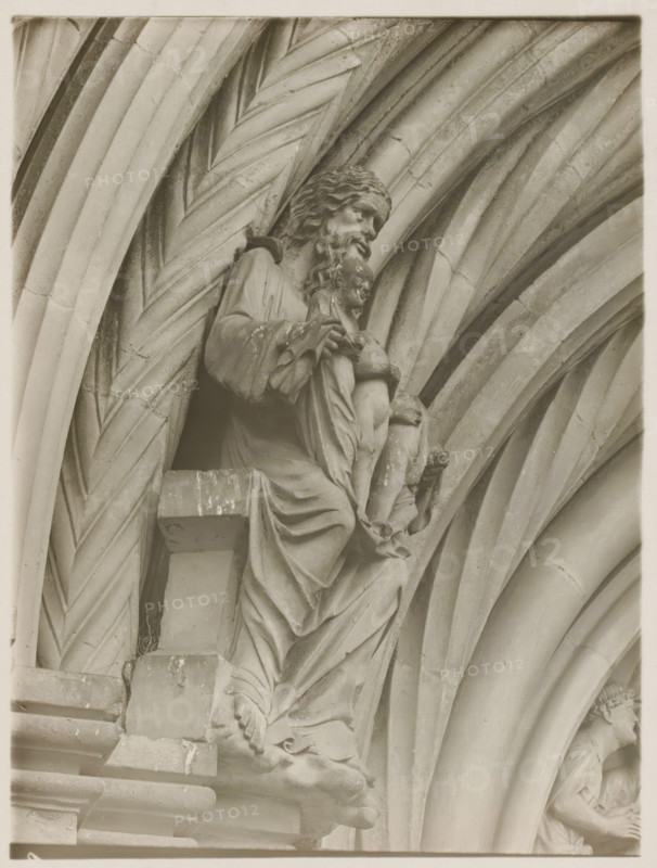 Fürstentor, Dasselbe, Abraham vl, Detail of the Fürstenportal in the cathedral of Bamberg, album page, photograph, This photo is part of an album., inscription: 'Kunsthist. Seminar, Marburg (Lahn), Photogr. Abteilung, Vervielfältigung, untersagt.', number: '109', Bamberg, 1900 - c. 1920, photographer, Bavaria, paper, baryta paper, gelatin silver print, developing gelatin silver print, height 238 mm x width 179 mm, church (exterior), Bamberg Cathedral, A stone sculpture of a robed, bearded man holding a smaller robed child is set within a series of carved, ribbed archways; the larger figure has wavy hair and a downward gaze, detailed drapery folds cascade over a ledge, and the child's legs and feet are visible as the adult's hands support the child; the surrounding arches display repeating curved and diagonal grooves and weathered surface texture, and a partial second figure appears in a recessed arch on the right.
