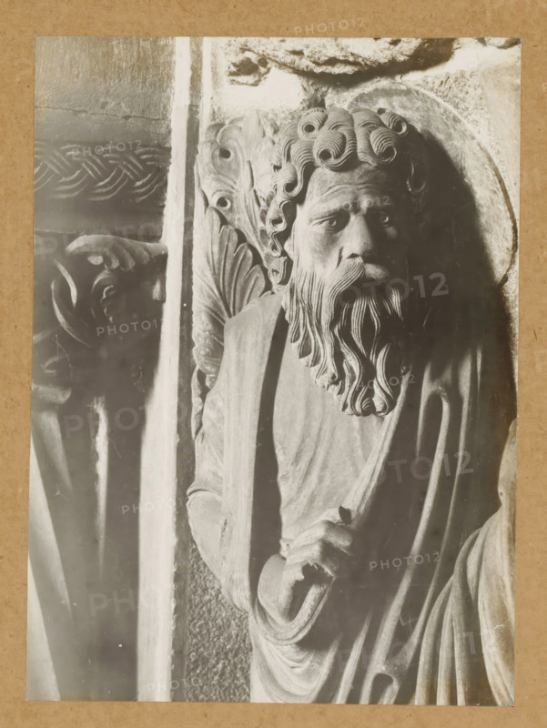 Georgenchorschranken, Prophetenrelief (n.SS) 1.Prophet v.li. (Kopf vv), Detail of the rood screen in the East Choir of Bamberg Cathedral, album page, photograph, This photo is part of an album., number: '118.', Bamberg, 1900 - c. 1920, photographer, Bavaria, paper, baryta paper, gelatin silver print, developed gelatin silver print, height 219 mm x width 160 mm, interior of church, Bamberg Cathedral, A close-up photograph of a carved stone figure showing a bearded man with curled hair and a flowing beard, his face turned slightly toward the viewer with a solemn expression, wearing draped robes and holding a staff or rod; ornate carved foliage and decorative patterns appear behind and beside him, and a second carved face is partially visible in shadow to the left.