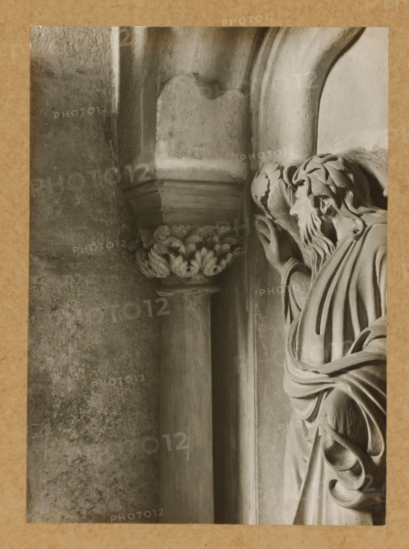 Detail of the rood screen in the East Choir of Bamberg Cathedral, Georgenchorschranken 6 Pvl (Dreiviertelprofil) u. Kapitelle, album page, photograph, This photo is part of an album., number: '123', Bamberg, 1900 - c. 1920, photographer, Bavaria, paper, baryta paper, gelatin silver print, gelatin silver developing print, height 222 mm x width 160 mm, interior of church, Bamberg Cathedral, A close-up black-and-white photograph of a carved stone figure set against architectural details, showing the right side of a bearded male figure with flowing hair and draped robes, his head turned slightly and his right hand raised near a decorative capital; the stone surfaces display smooth curves, carved folds, rounded columns, and a textured wall background, all framed by a narrow border of textured paper.