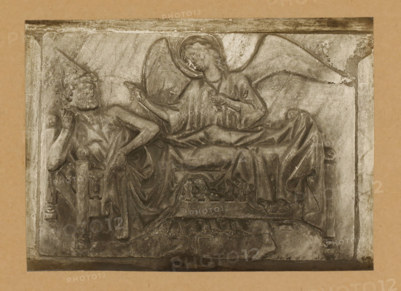 Grabmal, Clemens Tod, Detail of the tomb of Pope Clement II in the cathedral of Bamberg, album page, photograph, This photo is part of an album., number: '138.', Bamberg, 1900 - c. 1920, photographer, Bavaria, paper, baryta paper, gelatin silver print, developing gelatin silver print, height 150 mm x width 208 mm, Person, Clemens II, interior of church, Bamberg Cathedral, A weathered rectangular stone relief set against a plain background depicting two reclining human figures; one figure lies with an arm propped under the head and a pointed headpiece, the other figure is positioned nearby with large curved wings and a halo around the head, wearing draped garments and pointing with one hand while the other rests on the chest, folds of fabric and carved architectural elements appear beneath and around them, and the relief surface shows scratches, discoloration, and areas of wear.