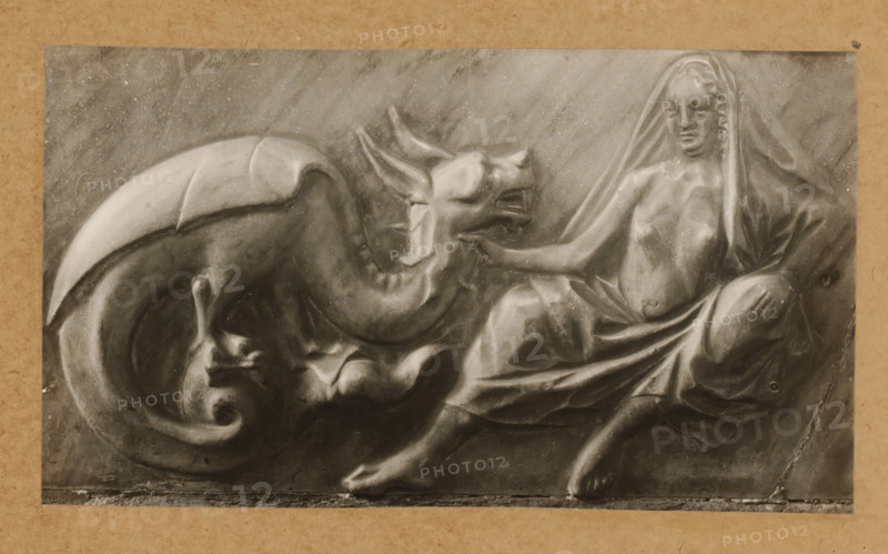 Detail of the tomb of Pope Clement II in the cathedral of Bamberg, Grabmal, Keuschheit, album page, photograph, This photo is part of an album., number: '139', Bamberg, 1900 - c. 1920, photographer, Bavaria, paper, baryta paper, gelatin silver print, developing gelatin silver print, height 127 mm x width 225 mm, Person, Clemens II, interior of church, Bamberg Cathedral, A carved relief showing a reclining draped female figure with a partially covered head and torso reaching toward a large reclining dragon-like creature with a curled tail and open mouth, all rendered in a smooth stone texture against a flat background and framed by a plain border.