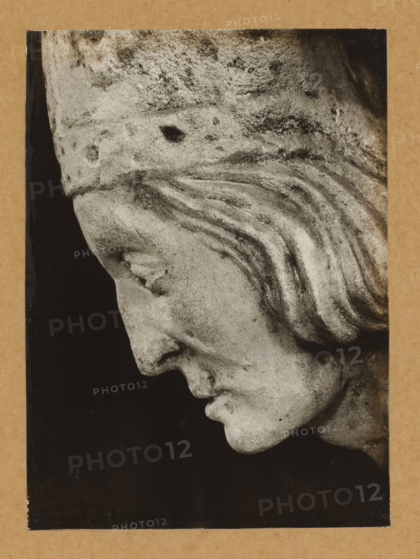 Sculpture of Friedrich I von Hohenlohe in the cathedral of Bamberg, Kreuzgang, Grabmal Friedrich v.Hohenlohe, Profil v. right, album page, photograph, This photo is part of an album., number: '155', Bamberg, 1900 - c. 1920, photographer, Bavaria, paper, baryta paper, gelatin silver print, developing gelatin silver print, height 225 mm x width 164 mm, Person, Friedrich I. von Hohenlohe, interior of church, Bamberg Cathedral, A close-up black-and-white photograph of a stone sculpture showing a downward-facing profile of a human head with carved hair in wavy strands, a pronounced brow and nose, closed eye, and a slightly open mouth, mounted on a rectangular frame with a dark background and a textured border.