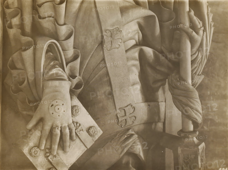 Sculpture of Albrecht von Wertheim in the cathedral of Bamberg, Kreuzgang, Grabmal Albert v.Wertheim, Hände u. Wall detail, album page, photograph, This photo is part of an album., inscription: 'Kunsthist. Seminar, Marburg (Lahn), Photogr. Abteilung, Vervielfältigung, untersagt.', number: '160', Bamberg, 1900 - c. 1920, photographer, Bavaria, paper, baryta paper, gelatin silver print, developing gelatin silver print, height 179 mm x width 239 mm, Person, Albrecht von Wertheim, interior of church, Bamberg Cathedral, A sepia-toned close-up of a stone sculpture showing draped fabric, a forearm and hand resting on a rectangular slab, and a vertical staff held by the opposite hand; the carved hand wears a ring and has a circular ornamental motif on the back, the slab bears raised floral medallions and decorative carved shapes, the drapery features deep folds and ruffled edges, and a carved band with ornamental ends crosses the torso area.