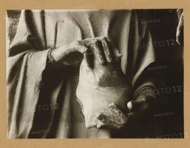 Adamspforte, Stephen (Hands), Detail of the Adamspforte in Bamberg Cathedral, album page, photograph, This photo is part of an album., number: '40.', Bamberg, 1900 - c. 1920, photographer, Bavaria, paper, baryta paper, gelatin silver print, developed gelatin silver print, height 169 mm x width 231 mm, Person, church (exterior), Bamberg Cathedral, A close view of a stone sculpture showing draped fabric and a pair of hands holding a rounded vessel, with visible surface weathering and cracks on the stone, soft shadows accentuating the folds of the garment, and textured worn areas on the fingers and vessel.