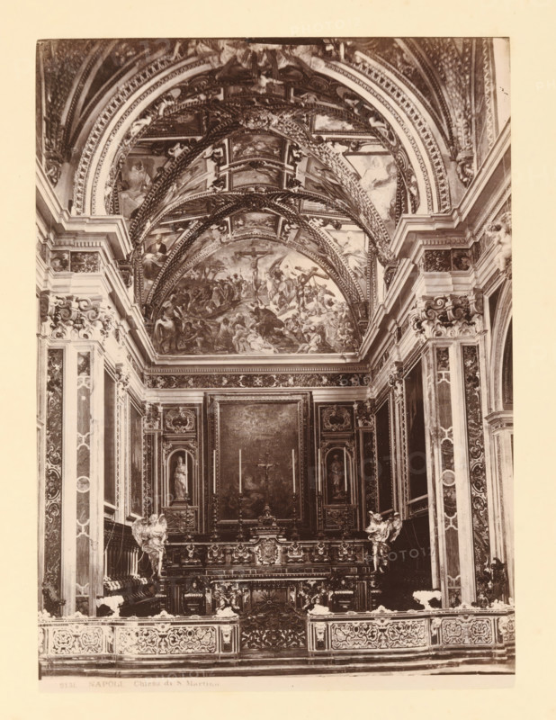 Interior of Chiesa di San Martino, Napoli Chiostro di S. Martino, album page, photograph, This photo is part of an album., workshop stamp: 'Giorgio Sommer, Largo Vittoria, Napoli', number: '8131', photographer: Giorgio Sommer, Naples, 1874 - in or before 1879, paper, albumen print, height 251 mm x width 182 mm, interior of church, A sepia-toned interior photograph showing an ornate chapel with a highly decorated vaulted ceiling featuring painted scenes and intricate arch moldings, flanked by elaborately carved pilasters and panels; a central altarpiece area with framed paintings and sculpted niches containing statues sits above a richly carved altar front with decorative reliefs and ornamental balustrades, and sculpted angelic figures positioned near the altar; patterns of marble, gilded ornamentation, and detailed architectural cornices run along the walls, while the lower foreground shows an ornamental railing with repeating carved motifs.