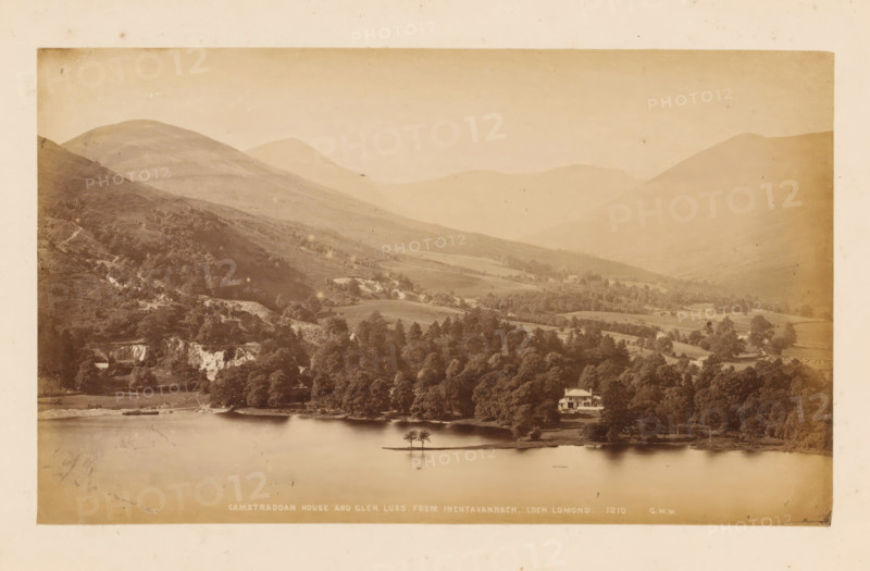 View of Loch Lomond, Glen Luss and Camstraddan House, Camstraddan House and Glen Luss from Inchtavannach, Loch Lomond, photograph, number: '1207, GWW', photographer: George Washington Wilson, Scotland, 1865 - 1880, paper, albumen print, height 116 mm x width 192 mm, landscapes with waters, waterscapes, seascapes (in the temperate zone), dale, valley, A wide sepia-toned landscape showing a calm body of water in the foreground with a small island holding a few trees near its center, a shoreline lined with dense trees and a light-colored house partially visible among the trees, rolling grassy hills rising behind the tree line, steeper wooded slopes and rocky outcrops on the nearer hills, and distant layered mountain ridges fading into the sky.