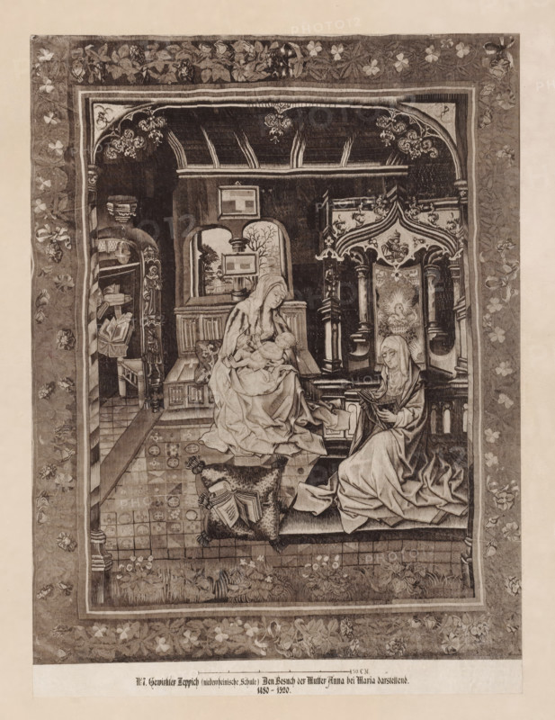 Carpet depicting Anna visiting Mary, 1480-1520, No. 7, photograph, photomechanical process, Gewirkter Teppich (Lower Rhine School) Dem Besuch der Mutter Anna bei Maria darstellend. 1480-1520., photographer: attributed to Johann Baptist Obernetter, 1869 - 1887, printer (person), Attributed to, pasteboard, paper, collotype, photoprint on paper on cardboard, height 281 mm x width 208 mm, tapestry, A rectangular woven scene framed by a wide floral border shows an interior with patterned floor tiles and ornate architectural elements, including carved columns and a decorative canopy. Two seated women in draped garments occupy the foreground; one holds an infant on her lap while the other looks down at a book she holds. Cushions with tassels and open books rest near their feet. A small animal lies on the tiled floor. Shelving with objects and a niche with framed scenes are visible in the background, along with foliage motifs and stylized floral decoration woven into the fabric. The overall im...