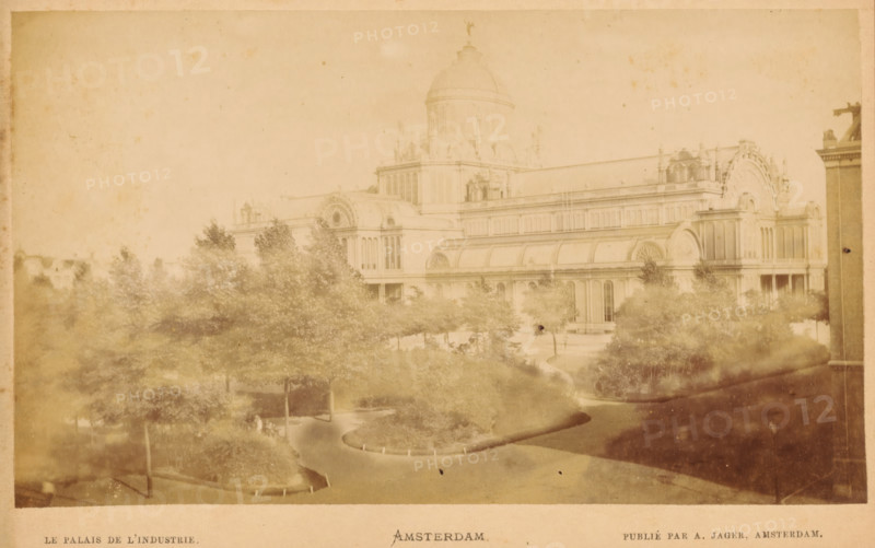 Exterior of the Palace of Industry in Amsterdam, Le palais de l'industrie Amsterdam., photograph, Amsterdam, publisher: Andries Jager, c. 1865 - c. 1880, Andries Jager, photographer, publisher, paper, pasteboard, albumen print, height 90 mm x width 157 mm, temporary exhibition, 'Salon', façade (of house or building), Palace of Industry, A sepia-toned photograph showing a large ornate building with domes and arched windows partially obscured by a park in the foreground. The park contains winding paved paths, planted beds, and many trees with leafy canopies. The building stretches horizontally across the scene with decorative architectural details and rounded roof sections. The image has a faded, aged appearance with light spots and darker edges.