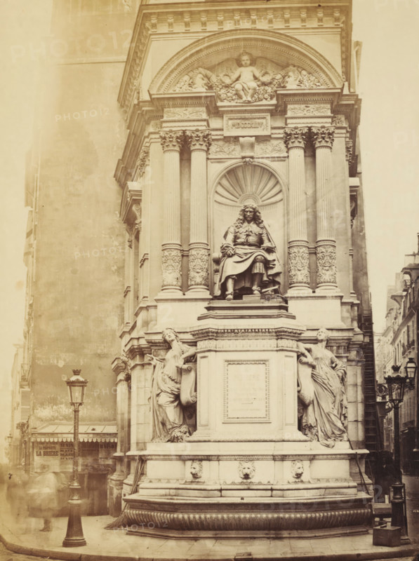 View of Fontaine Molière in Paris, photograph, Paris, 1850 - 1900, photographer, paper, pasteboard, albumen print, albumendruk, height 327 mm x width 501 mm, Person, Jean Baptiste Poquelin Molière, sculpture, ornamental fountain, Fontaine Molière, A sepia-toned photograph of an ornate stone monument set against a building facade, featuring a central seated statue of a robed figure within a recessed niche flanked by tall, fluted columns with decorative capitals and carved reliefs; above the niche is a semicircular pediment with a sculpted cherub and floral ornamentation. The monument rests on a multi-tiered plinth adorned with sculpted female figures draped in flowing garments on either side, carved lion head motifs near the base, and detailed moldings. Street elements visible include a tall lamppost in the foreground and parts of adjacent buildings lining a narrow street to the right, with awnings and rooftop features partially visible at the lower left and right edges. The overall sce...