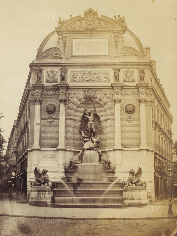 View of Fontaine Saint-Michel in Paris, photograph, Paris, 1860 - 1900, photographer, paper, pasteboard, albumen print, height 327 mm x width 501 mm, sculpture, ornamental fountain, the Archangel Michael fighting the dragon (devil, Satan), Fontaine Saint Michel, A large ornate stone façade fills the image, featuring classical columns, carved reliefs, and sculpted figures set into recessed arches, with a central statue of a winged figure standing atop a sculpted base from which water flows into a multi-tiered fountain; two winged lion-like creatures sit on pedestals flanking the fountain, and additional human statues stand in niches higher on the façade; decorative circular medallions and floral scrollwork appear on the upper sections, and buildings and narrow streets are visible receding on either side of the main structure.
