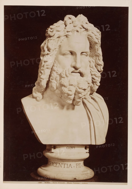 Giove d'Otricoli, Bust of Jupiter, Vatican, album page, photograph, This photo is part of an album., inscription: '1387 - ROMA - Giove d'Otricoli - Museo Vaticano - Anderson', photographer: James Anderson, Vatican Museums, after sculpture by anonymous, c. 1857 - c. 1875, after sculpture by, Vatican City, paper, albumen print, height 411 mm x width 288 mm, piece of sculpture, reproduction of a piece of sculpture, (story of) Jupiter (Zeus), A photograph of a marble bust showing a bearded male head with long wavy hair cascading around the face and onto the shoulders, the facial features carved with closed eyes and a prominent nose and full beard, the torso draped with a cloth over one shoulder, the bust set on a rounded pedestal with decorative molding, all shown against a dark background and framed by a lighter border.