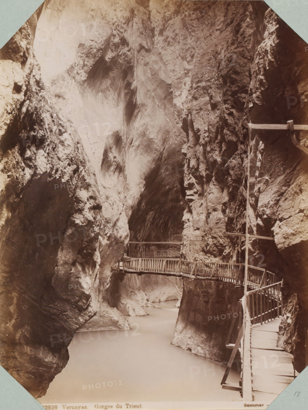 Bridge in the Trient Gorge, Vernayaz. Gorges du Trient, album page, photograph, This photo is part of an album., inscription: '13939 Vernayaz. Gorges du Trient. Sommer - Napoli', photographer: Giorgio Sommer, Trient (Switzerland), 1880 - 1890, paper, albumen print, height 255 mm x width 196 mm, ravine, chasm, abyss, canyon, Tall steep rock faces form a narrow gorge with smooth and jagged textures in shades of brown and grey, a pale river flowing at the base, and a series of wooden walkways and railings attached to the rock, winding along the cliff edge and crossing between rock walls.