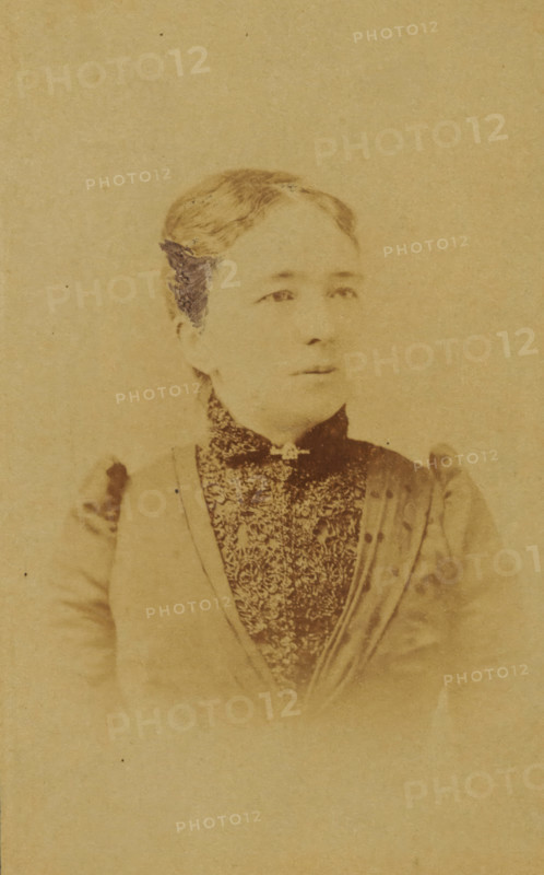 Portrait of a woman from the Marmelstein family, presumably the mother-in-law of AF Marmelstein, photograph, carte-de-visite, inscription: 'Photographie, Parisienne, H. van der Zijl, Nieuwendijk 60, over Raamskooi, Amsterdam., Please note the correct address.', annotation: 'Grandma', photographer: H. van der Zijl, Amsterdam, 1865 - 1900, paper, pasteboard, albumen print, albumendruk, height 104 mm x width 64 mm, historical persons not known by name - BB - woman, A faded sepia portrait of a woman shown from the chest up wearing a high-collared patterned garment and a darker outer layer with gathered shoulders, her hair pulled back and parted at the center, a small decorative element at the neck, and a neutral expression with eyes looking slightly to one side against a plain background.