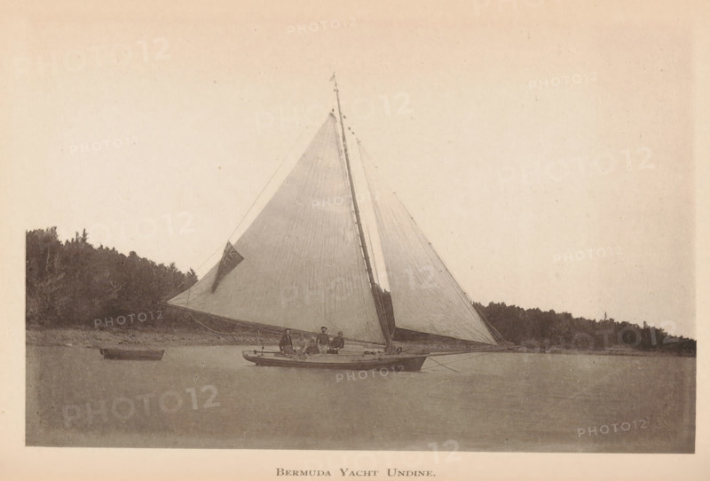 Bermuda yacht Undine, page, photomechanical print, photographer: James H. Stark, Bermuda, cliché maker: Photo-Electrotype Company, Boston (Massachusetts), c. 1879 - in or before 1884, North America, Massachusetts, paper, collotype, photoprint, height 90 mm x width 151 mm, ships (in general), A sepia-toned photograph of a sailboat on calm water with its large triangular sails raised, a small group of people seated on the deck, a smaller rowboat floating nearby, and a tree-lined shoreline in the background.