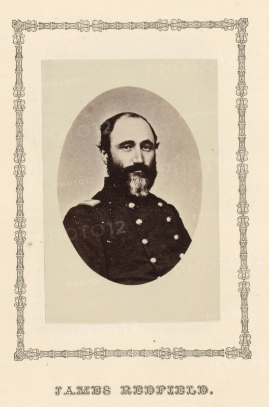 James Redfield, photograph, page, c. 1876 - in or before 1881, photographer, paper, albumen print, height 89 mm x width 59 mm, adult man, A sepia-toned oval portrait of a bearded man wearing a dark double-breasted uniform with visible buttons, mounted on a rectangular pale background and surrounded by an ornate decorative border on a light page.