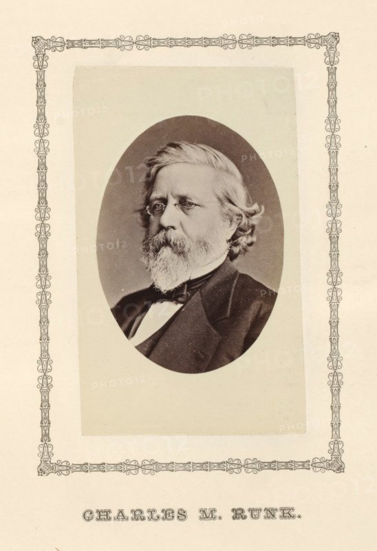Charles M. Runk, photograph, page, c. 1876 - in or before 1881, photographer, paper, albumen print, height 96 mm x width 59 mm, adult man, An oval black-and-white portrait of an older man with light hair and a full beard and mustache set against a plain background, the man wearing small round eyeglasses and a dark suit jacket with a bow tie, the portrait mounted on a light rectangular mat that is itself placed on a larger page decorated with an ornate narrow border along the edges.