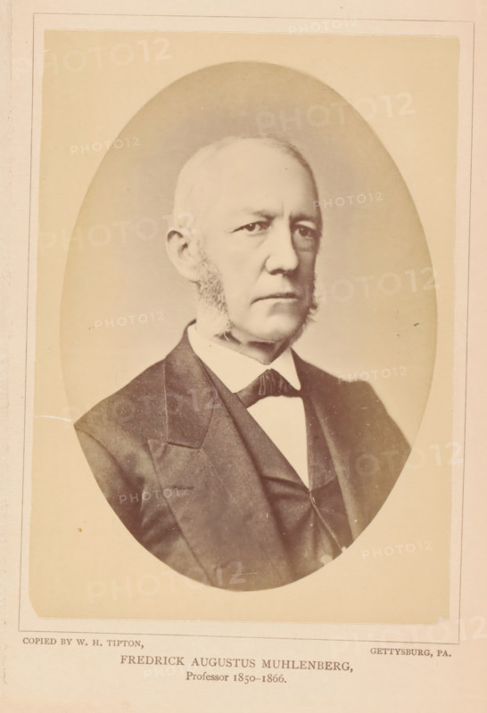 Fredrick Augustus Muhlenberg, photograph, page, photographer: William H. Tipton, Gettysburg, c. 1877 - in or before 1882, North America, Pennsylvania, paper, albumen print, height 146 mm x width 101 mm, Person, professor, A sepia-toned oval portrait of an older man shown from the chest up, wearing a dark suit jacket with a visible lapel, a vest, a white shirt with a high collar, and a dark bow tie; he has light-colored hair that is short and receding, prominent sideburns, a serious facial expression, and is looking slightly to the viewer's right, with a plain light background surrounding the oval and a pale rectangular border around the image.