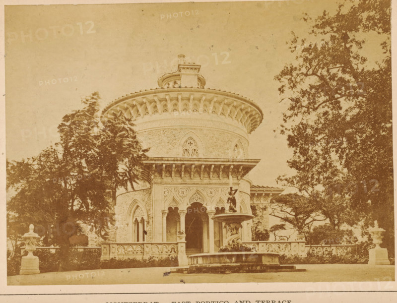 Montserrat-East portico ans terrace, View of a terrace and a portico of the Palácio de Monserrate near Sintra, photograph, page, Portugal, c. 1860 - in or before 1870, photographer, paper, albumen print, height 97 mm x width 132 mm, palace, terrace, gate, entrance, Palácio de Monserrate, A sepia-toned photograph showing a round ornate building with a wide decorative cornice and a smaller circular structure on top, flanked by tall trees; the façade features arched openings with columns, intricate carved patterns, and a balustraded terrace in front; a multi-tiered fountain with a statue stands near the entrance, and stone urns sit on pedestals along the terrace edges.