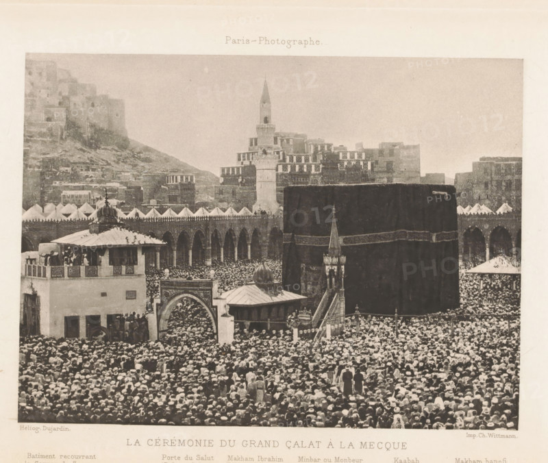 La cérémonie du grand Çalat à la Mecque, View of the Al-Masjid al-Haram in Mecca, page, photomechanical print, inscription: 'Batiment recouvrant, Tribune hanéfite', photographer: Félix Nadar (possibly), Mecca, cliché maker: Dujardin, France, printer (person): Charles Wittmann, c. 1883 - in or before 1893, printer (person), Saudi Arabia, paper, photoaquatint, height 118 mm x width 159 mm, temple, shrine, Islam, Mohammedanism, A large dark cuboid structure draped in cloth occupies the central foreground, surrounded by a dense crowd of people wearing head coverings that fill the visible plaza. In front of the cuboid is an ornate small building with a dome and a narrow staircase leading up to a covered platform, and an arched gateway with decorative patterns. To the left a multi-story building with a rooftop pavilion and balcony shows groups of people standing and leaning on railings. Behind the cuboid a long colonnaded arcade with repeated arches stretches horizontally, topped by a row of...