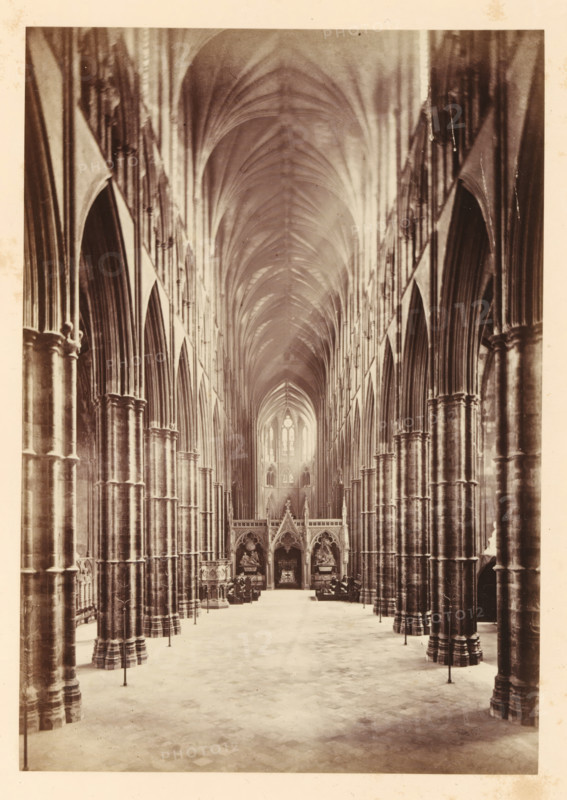 The nave in Westminster Abbey, looking east, photograph, page, photographer: John Harrington, c. 1864 - in or before 1869, paper, albumen print, height 188 mm x width 131 mm, interior of church, abbey, monastery, convent, Roman Catholic church, parts of church interior: nave, London, Westminster Abbey, A tall, vaulted interior with a long central aisle flanked by rows of massive stone columns and pointed arches, the ceiling forming a ribbed series of curved vaults that converge toward a distant, illuminated window; ornate carved screens and sculptural elements sit at the far end of the aisle, with seating and decorative fixtures along the sides, and a patterned stone floor stretching forward from the foreground.