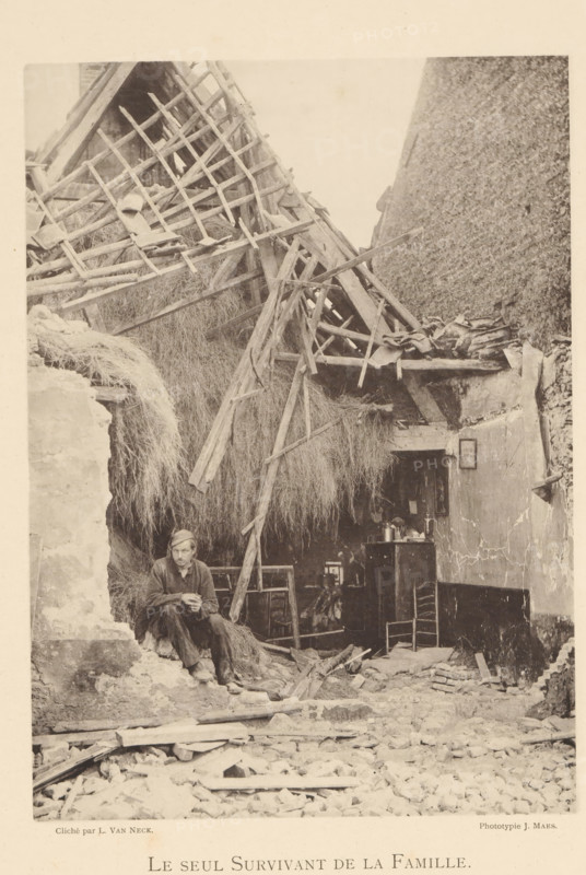 Le seul survivant de la famille, Man in a destroyed house after an explosion of a munitions factory in Oosterweel near Antwerp in 1889, page, photomechanical print, number: '12', photographer: L. van Neck, Oosterweel, cliché maker: anonymous, Belgium, printer (person): J. Maes (possibly), Antwerp, 1889, printer (person), paper, collotype, photoprint, height 230 mm x width 165 mm, Image on page 12., ruin of a building, architecture, Explosion of a munitions factory in Oosterweel in 1889, A sepia-toned scene shows a partially collapsed thatched structure with broken wooden beams and latticework leaning inward and strewn across a large mass of straw or hay; debris and rubble cover the foreground while a man sits on a rough stone ledge near the left, wearing a cap and simple clothing and holding his hands together, with a somber posture; behind and to the right of him an interior space is visible with a small table or cabinet holding assorted vessels and objects, a chair pushed against a w...