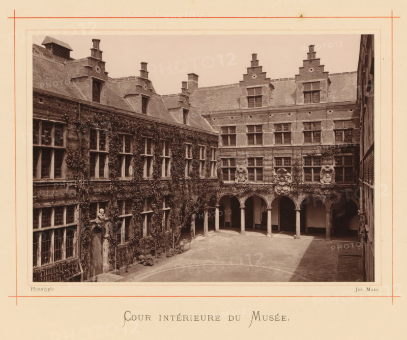 Courtyard of the house of Christoffel Plantijn, Cour intérieure du Musée, page, photomechanical print, maker: Joseph Maes, Antwerp, c. 1873 - in or before 1878, paper, Woodburytype, height 118 mm x width 164 mm, courtyard, A sepia photograph of a rectangular stone courtyard surrounded by multi-story brick and stone buildings with steep tiled roofs and stepped gables, featuring rows of rectangular windows with small panes and window frames, arched openings supported by columns along one side opening into a covered gallery, decorative stone medallions and sculpted reliefs above some arches, climbing vines covering large portions of one facade and winding around windows and doors, a cobbled or paved central ground area with a curved paving pattern near the foreground, and a framed border around the image.