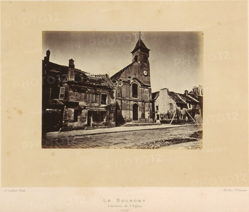 View of the church of Le Bourget after the destruction by the Paris Commune, Le Bourget. Exterieur de l'Eglise, photograph, page, address: '31, Rue St. Lazare', number: '(No. 95)', photographer: Alphonse-Justin Liébert, Le Bourget, 1871 - 1872, Alphonse-Justin Liébert, photographer, paper, albumen print, albumendruk, height 99 mm x width 135 mm, ruin of church, monastery, Paris Commune (1871), A sepia-toned photograph shows a street scene with a stone church featuring a tall bell tower topped by a pointed roof and a round clock face on the tower wall, flanked by worn buildings with shuttered windows and pitched roofs, some roof sections appearing damaged or missing tiles, a cobblestone road in the foreground, scaffolding and wooden supports leaning against one of the adjacent buildings, and a pale border surrounding the image.