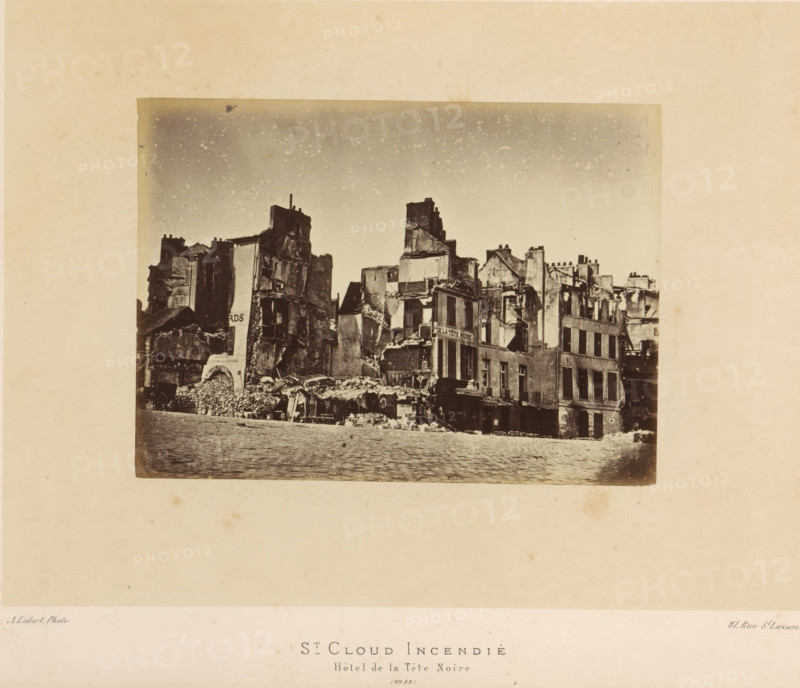 St. Cloud Incendié. Hôtel de la Tête Noire, View of the Hôtel de la Tête Noire in Saint-Cloud after the fire by the Paris Commune, photograph, page, number: '(No. 55)', address: '31, Rue St. Lazare', photographer: Alphonse-Justin Liébert, Saint-Cloud, 1871 - 1872, paper, albumen print, height 98 mm x width 135 mm, ruin of a building, architecture, civic architecture, edifices, dwellings, Paris Commune (1871), A sepia-toned photograph centered on a wide scene of damaged multi-story buildings with exposed interiors and broken façades, rubble piled along the ground in front, collapsed roofs and crumbling walls, a cobblestone street in the foreground, scattered architectural debris and makeshift coverings among the ruins, remnants of storefronts and window openings, chimneys and partial upper walls silhouetted against a speckled sky, all mounted on a large pale mat with a blank margin surrounding the image.
