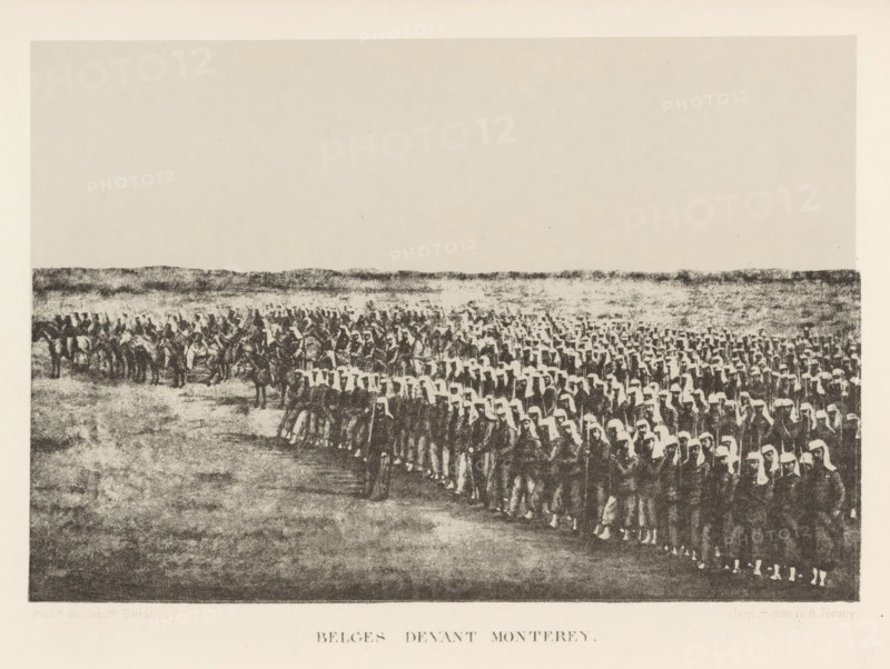 View of army troops, Belges Devant Monterey, page, photomechanical print, photographer: Capitaine Louis Delaunoy, Mexico, cliché maker: Simonau & Toovey (possibly), Brussels, c. 1867 - in or before 1872, printer (person), North America, paper, photolithography, height 114 mm x width 169 mm, assembling of military forces, mobilization, troop concentration, A wide landscape view with a large assembled group of people filling the lower half of the image, arranged in many orderly rows and wearing light head coverings and dark garments, with some individuals on horseback to the left and a low, textured horizon line stretching across the middle; the upper portion is an open, pale sky, and the ground in the foreground shows a mottled, grainy texture.