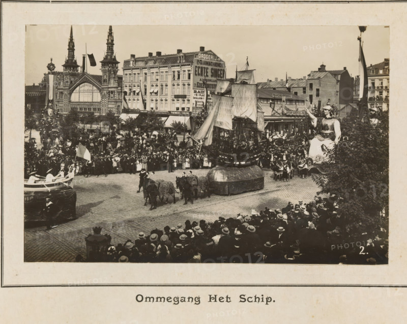 Ommegang the ship, photograph, page, Antwerp, c. 1899, photographer, paper, printing, height 98 mm x width 154 mm, civic architecture, edifices, dwellings, animal traction, animal-drawn vehicle (carriage etc.), festivities (decorated float, wagon, festive activities), A large street scene shows a crowded parade with many people lining cobbled streets and balconies, spectators wearing hats filling the foreground and midground. Decorative floats move along the street, including a large ship-like float with tall sails and rigging, and another float resembling a seated figure in ornate costume raising one arm. Costumed participants accompany the floats, some riding decorated animals harnessed in pairs, and others walking beside the displays. Behind the crowd are multi-story buildings with ornate facades and towers, shopfronts, awnings, and flags displayed on poles. Trees and ornamental lamp posts are visible near the street, and portions of the scene are framed by darker foliage at the rig...