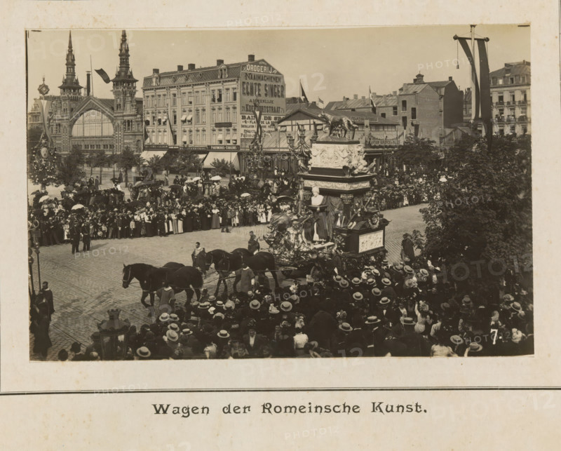 Wagon of Roman art, photograph, page, Antwerp, c. 1899, photographer, paper, printing, height 98 mm x width 152 mm, civic architecture, edifices, dwellings, animal traction, animal-drawn vehicle (carriage etc.), festivities (decorated float, wagon, festive activities), A crowded street scene shows a large ornate float pulled by horses moving through a densely packed throng of people wearing hats and coats, many holding parasols, with a corner of the float featuring sculpted figures and a bust and decorative reliefs; behind the crowd there are multi-story buildings with decorative facades, a large building with tall spires and an arched window, a row of storefronts with awnings, and flagpoles with banners; trees and lamp posts punctuate the scene and people line the sidewalks and upper windows overlooking the procession.
