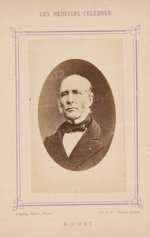 Portrait of Alfred-Louis-Dominique Richet, Richet, photograph, page, inscription: '(Publication de la Revue de literature médicale du, No.', photographer: Pierre Petit, c. 1871 - c. 1879, paper, albumen print, albumendruk, height 91 mm x width 57 mm, Person, Alfred-Louis-Dominique Richet, historical persons, adult man, An oval sepia photograph of an older man mounted on a pale rectangular card with decorative purple border lines and corner flourishes, showing the man from the chest up wearing a dark coat, a high white collar, and a bow tie, with light-colored hair combed back and muttonchop sideburns, a serious facial expression, and a plain light background within the oval.