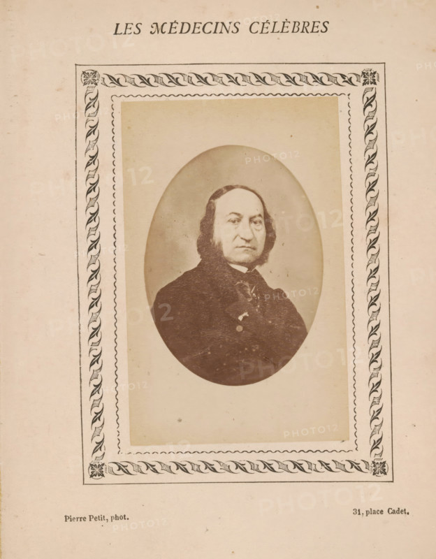 Portrait of an unknown man, photograph, page, inscription: 'Publication de la Revue de literature médicale, du docteur Felix Bremond, 20, Passage Saulnier, 3e année.) - No.', number: '79', photographer: Pierre Petit, c. 1871 - c. 1879, paper, albumen print, albumendruk, height 82 mm x width 51 mm, historical persons, adult man, A sepia-toned portrait of a middle-aged man with a high forehead and dark, shoulder-length hair framing his face, shown from the chest up inside an oval vignette; he wears a dark coat and a necktie with a visible collar and has a neutral facial expression. The oval portrait is set within a rectangular mat bordered by a decorative rope-and-leaf patterned frame with corner floral motifs, all printed on aged, off-white paper with small spots and uneven discoloration.