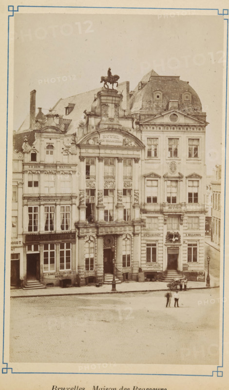 View of the Brewers' House in Brussels, Bruxelles. Maison de Brasseurs, photograph, page, Brussels, c. 1875 - c. 1880, photographer, paper, albumen print, height 170 mm x width 102 mm, street (city(-scape) with figures, staffage), façade (of house or building), A sepia-toned photograph of an ornate row of multi-story stone buildings with decorative facades and tall windows, the central building featuring large columns, sculpted ornamentation, and an arched entrance topped by an equestrian statue on its roof; adjacent buildings show varied rooflines, dormer windows, and sculpted detailing, with storefronts and entrances at street level, window curtains visible in some windows, and awnings over lower windows; a cobbled street runs in front of the buildings, where a few people stand together near a small cart and a lamppost, and additional lampposts are positioned along the sidewalk.