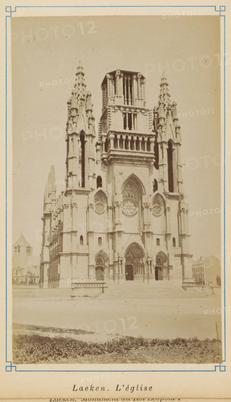 View of the Church of Our Lady in Laeken, Laeken. L'église, photograph, page, Laeken, c. 1875 - c. 1880, photographer, Brussels, paper, albumen print, albumendruk, height 171 mm x width 103 mm, church (exterior), A sepia-toned photograph of a large Gothic-style church façade with twin ornate spires flanking a central tower, pointed arches, carved stonework, circular rose windows, and three arched doorways at the main entrance, set behind a low platform and steps with a grassy foreground and framed by a thin decorative border.