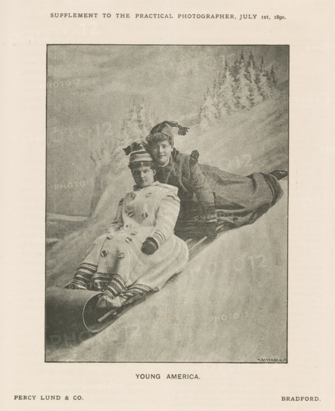 Young America, Portrait of two unknown women on a sled, page, photomechanical print, inscription: 'SUPPLEMENT TO THE PRACTICAL PHOTOGRAPHER, JULY 1st, 1890.', maker: Heinrich Riffarth, maker: Percy Lund & Co., Bradford (Pennsylvania) (possibly), c. 1885 - in or before 1890, North America, Pennsylvania, paper, autotype, height 133 mm x width 101 mm, historical persons not known by name - BB - woman, sleigh, sledge (non-sport), A monochrome printed photograph framed on a page shows two women seated on a sled on a snowy slope with a backdrop suggesting trees on a hillside. The woman in front wears a light-colored coat with decorative buttons, striped leggings, dark gloves, and a hat with a band; her legs are extended and her feet rest on the sled. The woman behind leans forward over the front woman's shoulder and wears a darker long coat, gloves, and a hat with a long tassel that drapes over her head. The sled appears wooden with metal runners visible at the front. The photograph is borde...