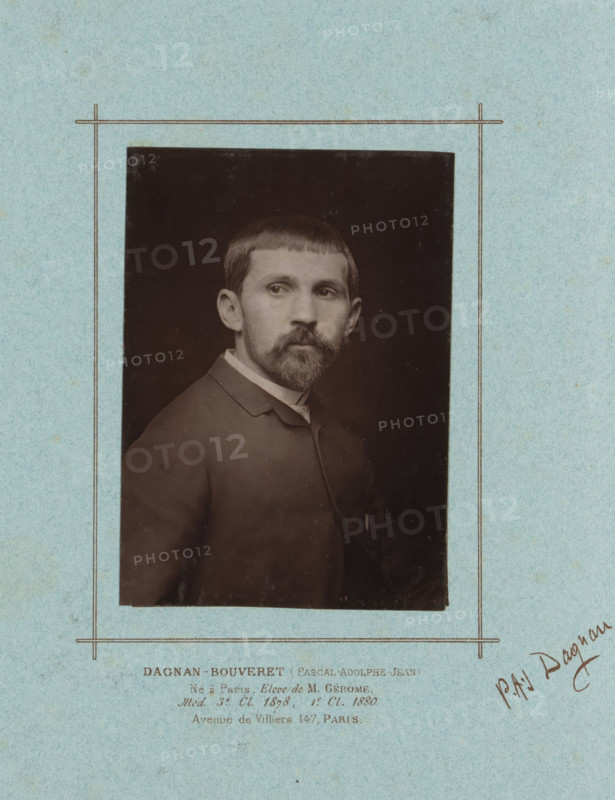 Portrait of Pascal-Adolphe-Jean Dagnan-Bouveret, page, photomechanical print, inscription: 'DAGNAN-BOUVERET (Pascal-Adolphe-Jean), Né à Paris. Elève de M. Gérôme, Med. 3rd. Cl. 1878, 1st. Cl. 1880., Avenue de Villiers, 147, Paris.', signature: 'PAJ Dagnan.', cliché maker: Lemercier (possibly), c. 1879 - in or before 1884, photographer, paper, Woodburytype, Woodburytypie, height 138 mm x width 99 mm, Person, Pascal-Adolphe-Jean Dagnan-Bouveret, historical persons, portrait, self-portrait of painter, A sepia portrait of a man mounted on textured light blue paper with a simple thin rectangular border drawn around the photograph; the man faces slightly to his left with short straight hair and a trimmed mustache and beard, wearing a dark jacket with a visible collar and a light shirt underneath, and the photograph shows a dark background behind him.