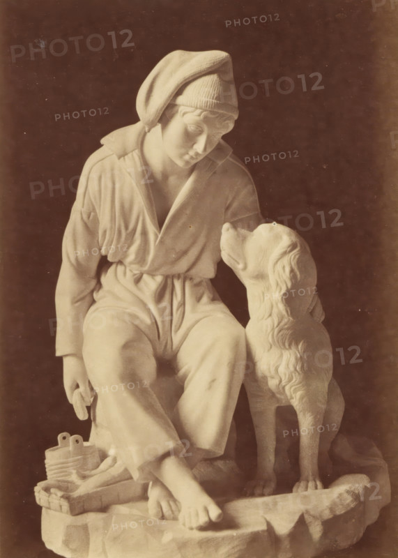 Sculpture of a boy and a dog by Leopold Borbone, photograph, This photograph is part of a cover with 18 photographs on 18 sheets and 14 text sheets., photographer: Grillet jeune, c. 1854 - in or before 1859, paper, albumen print, height 162 mm x width 115 mm, piece of sculpture, reproduction of a piece of sculpture, boy (child between toddler and youth), dog, A sepia-toned photograph of a seated statue depicting a person wearing a loose garment and a soft cap, head tilted downward and gazing toward a dog sitting beside them, the dog looking up at the person; the person’s bare feet rest on a textured base and a small basket and coiled object sit near their feet; the scene is set against a dark rectangular background framed by multiple light and dark borders on a light paper mount.