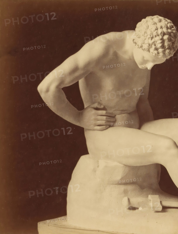 Sculpture of a man and a sword by Leopold Borbone, photograph, This photograph is part of a cover with 18 photographs on 18 sheets and 14 text sheets., photographer: Grillet jeune (possibly), c. 1854 - in or before 1859, paper, albumen print, height 139 mm x width 192 mm, piece of sculpture, reproduction of a piece of sculpture, hacking and thrusting weapons: sword, man (showing himself) undressed, quasi-nude, A framed photograph of a reclining marble statue shown from the torso upward against a dark background, with a pale border and decorative double-line matting around it; the statue shows a muscular arm bent with a hand resting on the abdomen, a second arm tensed, a curled head with detailed hair, and part of a plinth visible at the side, all rendered in soft beige and sepia tones.