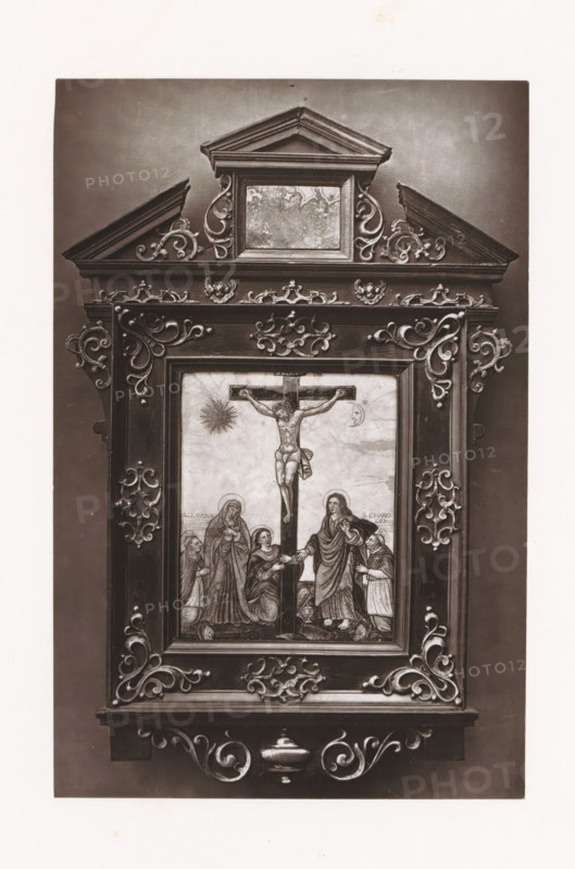 Enamel image of the crucifixion of Christ, displayed during the Exposition Rétrospective of 1873 in Tours, France, page, photomechanical print, maker: Gabriel Blaise, Tours, 1873, paper, Woodburytype, Woodburytypepie, height 193 mm x width 127 mm, picture, painting, temporary exhibition, 'Salon', crucified Christ, with particular persons under the cross, enamelling, applied arts, Period, 1873-05-03 - 1873-05-25, A tall ornate rectangular wooden frame with carved scrollwork surrounds a painted scene of a crucifixion; the frame has a pediment at the top with a small recessed panel and decorative curving motifs on either side, layered molding and symmetrical carved flourishes running along the borders. The central painted panel shows a figure on a cross with an expressive posture, a radiant circular shape to one side and a smaller crescent shape on the other, and several robed figures gathered at the base of the cross in varied standing and kneeling poses. The frame displays corner and si...