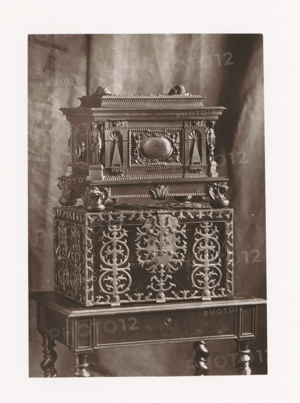 Two chests, displayed during the 1873 Exposition Rétrospective in Tours, France, page, photomechanical print, maker: Gabriel Blaise, Tours, 1873, paper, Woodburytype, Woodburytypepie, height 168 mm x width 117 mm, temporary exhibition, 'Salon', chest, coffer (wood and other phytogenic material), Period, 1873-05-03 - 1873-05-25, A photograph of a decorative chest displayed on a small wooden table, showing intricate carved patterns and ornamental details; the chest features ornate scrollwork panels with symmetrical floral and circular motifs on its sides, a patterned base with rounded feet, and a raised upper section adorned with sculpted figures, fluted columns, a central oval cartouche, and beaded molding; the table beneath has a drawer front, turned legs, and a polished finish, all set against a softly draped fabric backdrop.